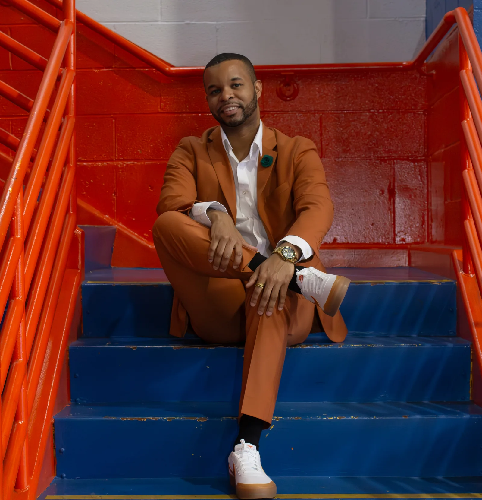 Merrick Lee, strategic growth advisor and Fractional CMO in New York City, seated on stairs in a rust suit