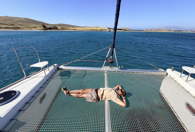 Merrick Lee relaxing on a catamaran net near Rinia in the Greek islands, turquoise sea all around