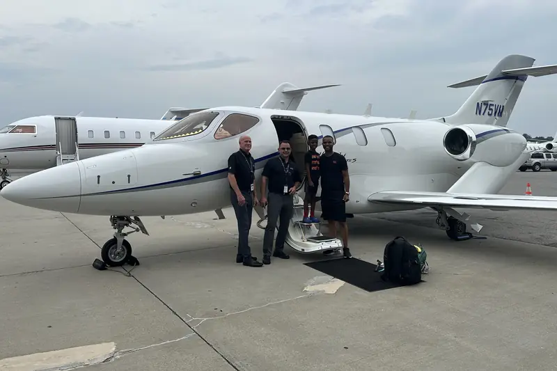 Merrick Lee and Maddox with two crew members on the tarmac beside a white private jet, its stairs down