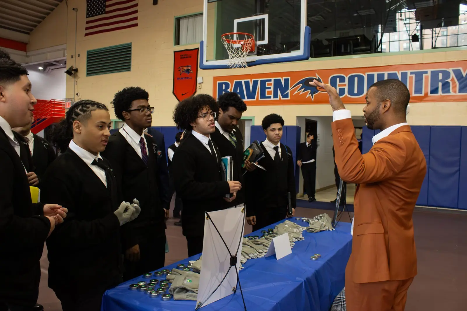 Merrick Lee Jr., in an orange suit, talking with a row of students at his career day table in New York City